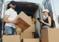 Courier business owners loading cardboard boxes into a delivery van while checking orders on a tablet