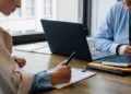 Business owner taking notes across a desk from an advisor with a laptop and folders while reviewing a business address change