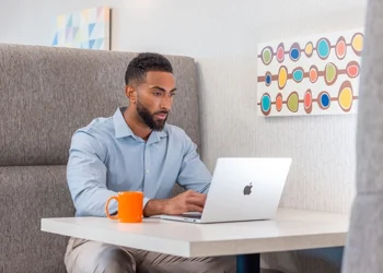 Business professional using a laptop at a private workspace booth inside a modern business center