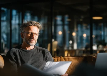 A focused professional reviews documents on a leather sofa inside a modern, warmly lit office space — the kind of presence a business address should project