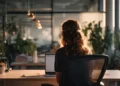 Woman sitting at a desk with a laptop in a modern office with plants and warm lighting, representing a professional using a telephone answering service