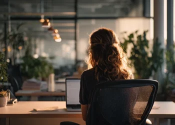 Woman sitting at a desk with a laptop in a modern office with plants and warm lighting, representing a professional using a telephone answering service
