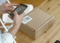 Person scanning a QR code shipping label on a cardboard package with a smartphone