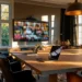 The Future of Meeting Rooms- 2026 Trends | Alliance Virtual Offices Modern meeting room with a large wooden conference table, laptops, and a wall-mounted screen showing a video call grid, lit by natural light from tall windows