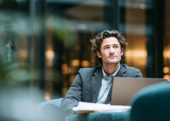 Professional man in a blazer working on a laptop in a modern, upscale office lounge surrounded by greenery and warm ambient lighting
