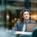 Alliance Virtual Offices vs Opus Virtual Offices- 2026 Service Cost Comparison | Alliance Virtual Offices Professional man in a blazer working on a laptop in a modern, upscale office lounge surrounded by greenery and warm ambient lighting