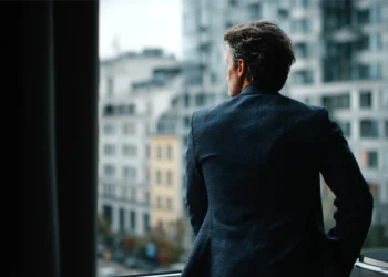 Business consultant looking out an office window at a city skyline, considering expansion to a new U.S. market