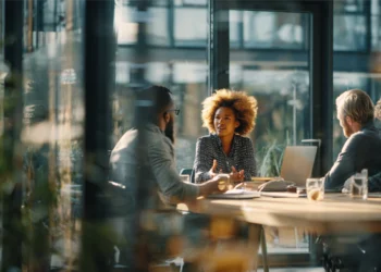 Three professionals having a meeting in a modern glass-walled conference room, representing meeting room rental options for businesses.