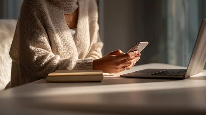 10 Best Virtual Receptionist Services for US Mobile Professionals | Alliance Virtual Offices Mobile professional checking her smartphone at a desk with a laptop and notebook, illustrating how virtual receptionist services support US professionals on the go.