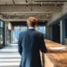 Virtual Mailbox vs Virtual Office- When to Upgrade Your Business Address | Alliance Virtual Offices Businessman in dark suit standing at a wooden reception desk in a modern office lobby with concrete walls and large windows