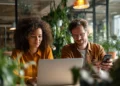 Two remote professionals collaborating at a laptop in a modern coworking space filled with green plants, representing virtual office solutions for distributed teams.