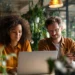 Virtual Office Solutions for Remote Teams- Your 2026 Guide to Working Professionally from Anywhere | Alliance Virtual Offices Two remote professionals collaborating at a laptop in a modern coworking space filled with green plants, representing virtual office solutions for distributed teams.