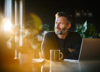 Small business owner sitting at a desk with a laptop and coffee mug, looking confident while considering AI answering service options for his company