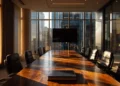 Professional conference room with a polished wood table, black leather chairs, a wall-mounted screen, and floor-to-ceiling windows overlooking a city skyline at golden hour.