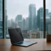 Laptop and coffee mug on a wooden desk in a high-rise office with a panoramic city skyline view through floor-to-ceiling windows on a cloudy day