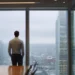 How to Book Meeting Rooms in the UK and Canada | Alliance Virtual Offices Businessman standing at floor-to-ceiling windows in a high-rise meeting room overlooking a city skyline
