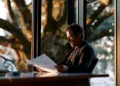 Business owner reviewing financial documents at a desk with laptop near large windows, researching PAYDEX score and business credit reports