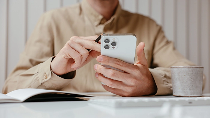 Phone Forwarding- How to Forward Your Calls to Another Number | Alliance Virtual Offices Person checking forwarded business calls on a smartphone at a desk with a notebook and coffee mug