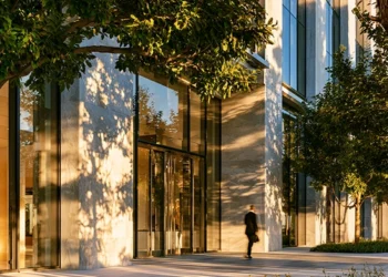 Professional walking past a modern glass office building with trees and natural light, representing virtual office cost savings compared to traditional leases