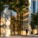 Professional walking past a modern glass office building with trees and natural light, representing virtual office cost savings compared to traditional leases