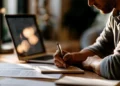 Independent contractor writing notes beside a laptop and paperwork at a desk