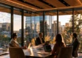 Four professionals meeting around a table in a high-rise conference room with floor-to-ceiling windows overlooking a Houston skyline at sunset