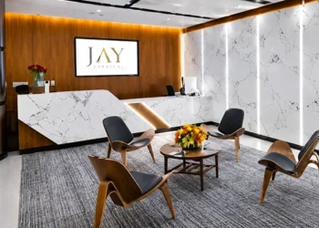 Reception and waiting area with a marble front desk, wood-panel wall, backlit marble panels, and four molded wood chairs around a round coffee table
