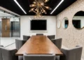 Meeting room with wood conference table, gray chairs, wall-mounted screen, and round mirrors on a textured stone wall