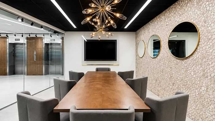 Conference Room Rental Atlanta- How to Book Professional Meeting Space | Alliance Virtual Offices Meeting room with wood conference table, gray chairs, wall-mounted screen, and round mirrors on a textured stone wall