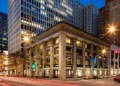 Chicago street corner at night: classical columned building with ground-floor shops and office towers behind