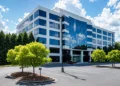 Modern five-story office building with blue glass facade and landscaped parking lo