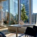 Sunlit private office with a laptop on a height-adjustable desk, navy velvet chairs, and floor-to-ceiling windows overlooking a city street