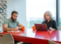 Two professionals working at a red conference table in a modern Alliance Virtual Offices meeting room with floor-to-ceiling windows