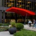 Pedestrians walking past the landscaped plaza entrance of a modern office tower with a bright red canopy