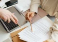 Two people reviewing business documents at a desk with a laptop, notepad, and printed paperwork