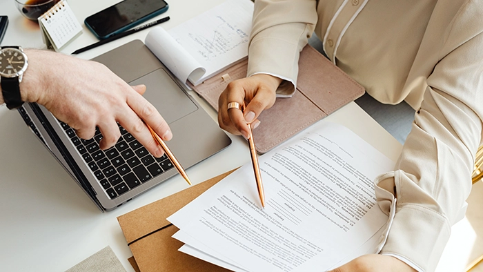 New York Registered Agent- Requirements Costs Rules | Alliance Virtual Offices Two people reviewing business documents at a desk with a laptop, notepad, and printed paperwork