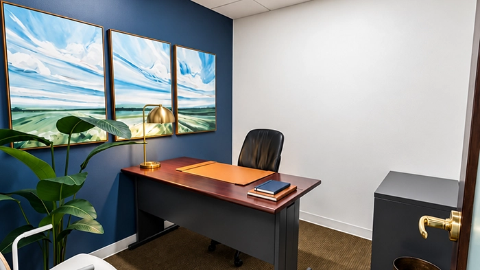 Best Answering Services for Insurance Agents | Alliance Virtual Offices Private day office with a wood desk, black leather chair, brass desk lamp, and coastal artwork on a navy accent wall