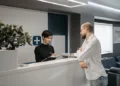 Receptionist taking notes at a front desk while greeting a visitor in a modern business center lobby