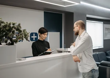 Receptionist taking notes at a front desk while greeting a visitor in a modern business center lobby