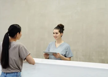 Veterinary receptionist in scrubs holding a tablet and greeting a client at the front desk of a clinic
