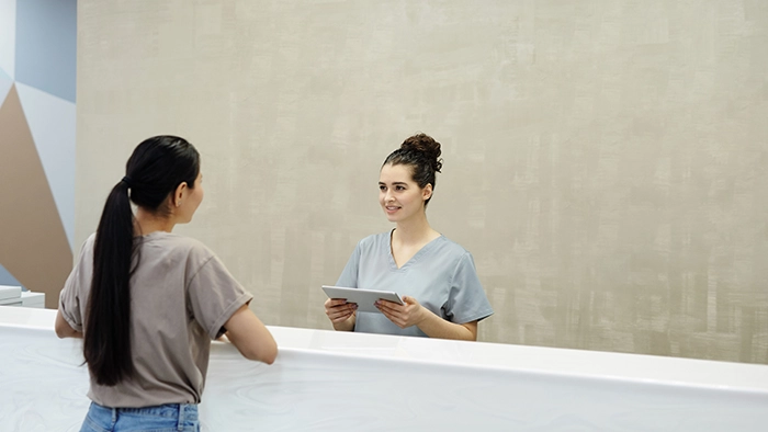 Best Veterinary Answering Services | Alliance Virtual Offices Veterinary receptionist in scrubs holding a tablet and greeting a client at the front desk of a clinic