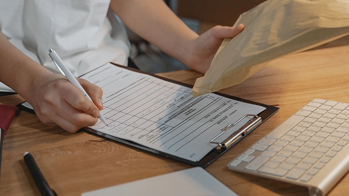Can You Use a Registered Agent Address as Your Business Address_ | Alliance Virtual Offices Person filling out a business registration form on a clipboard while holding a mail envelope at a desk