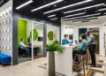 Modern coworking space with a glass-walled private office, standing-height table, and professionals working on laptops